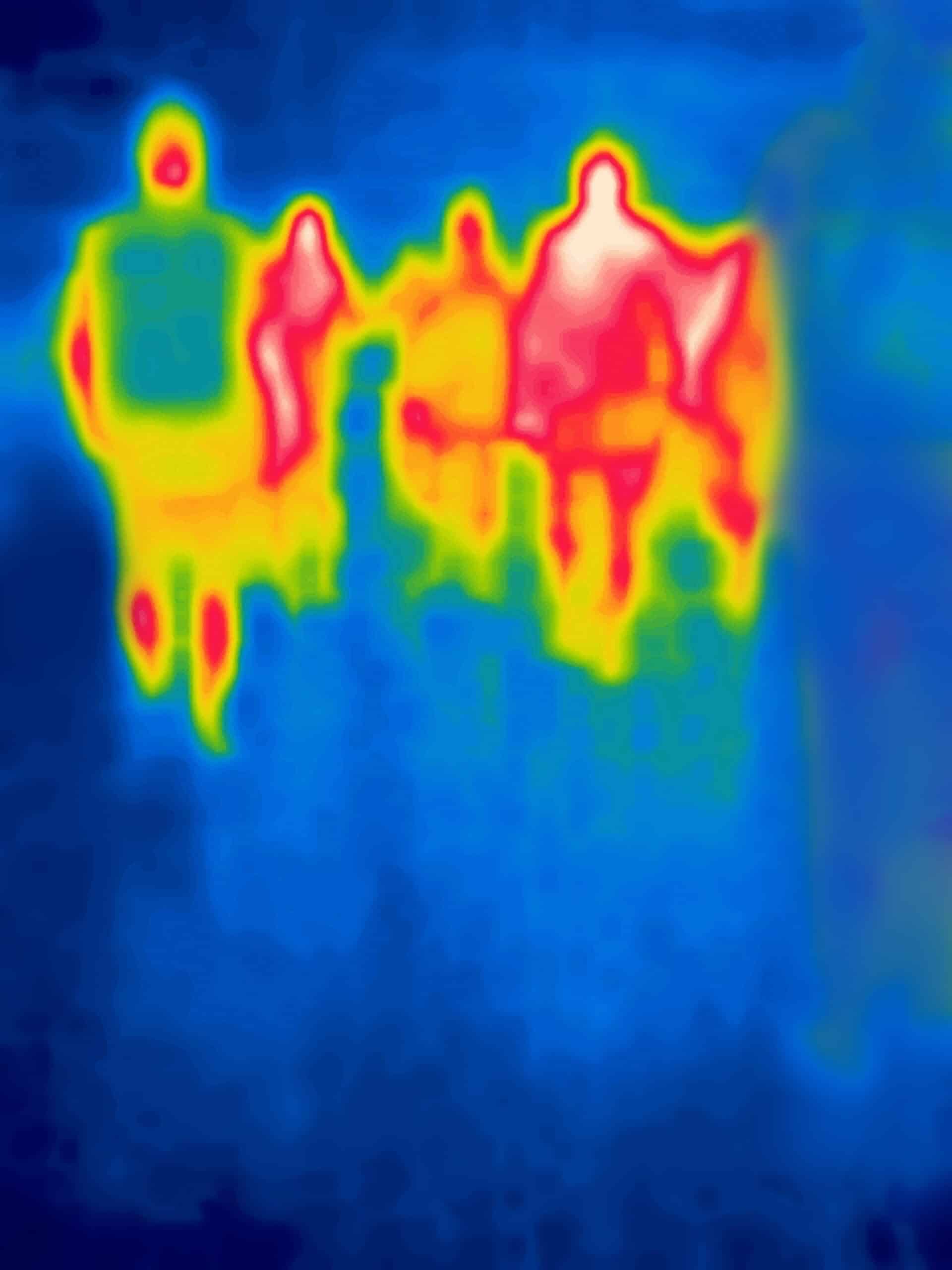 Image thermique montrant quatre silhouettes humaines chaudes (rouge, jaune, vert) sur un fond bleu froid, probablement debout ou assises ensemble.