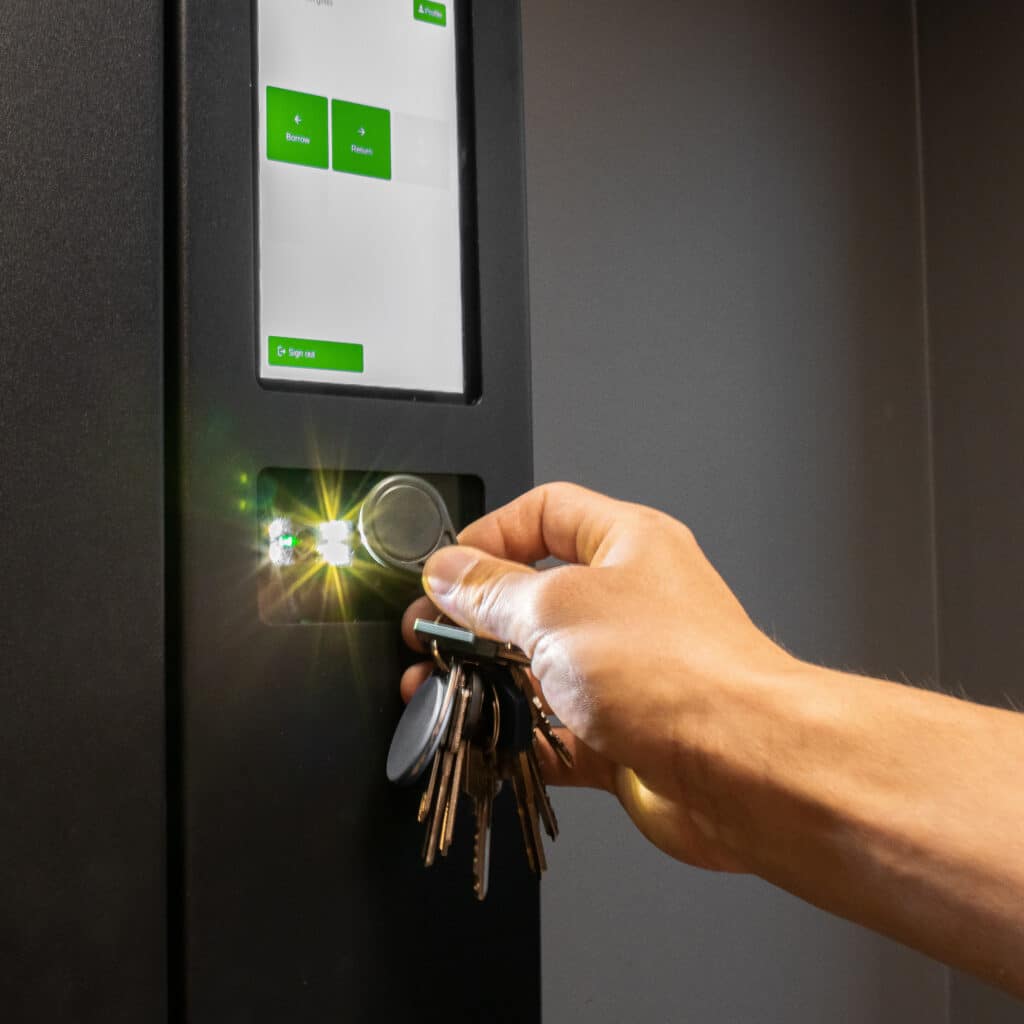 Borne accès clés : emprunt, retour avec badge Main présentant un trousseau de clés avec un badge à un lecteur lumineux sur une borne avec options 'Borrow' et 'Return'.
